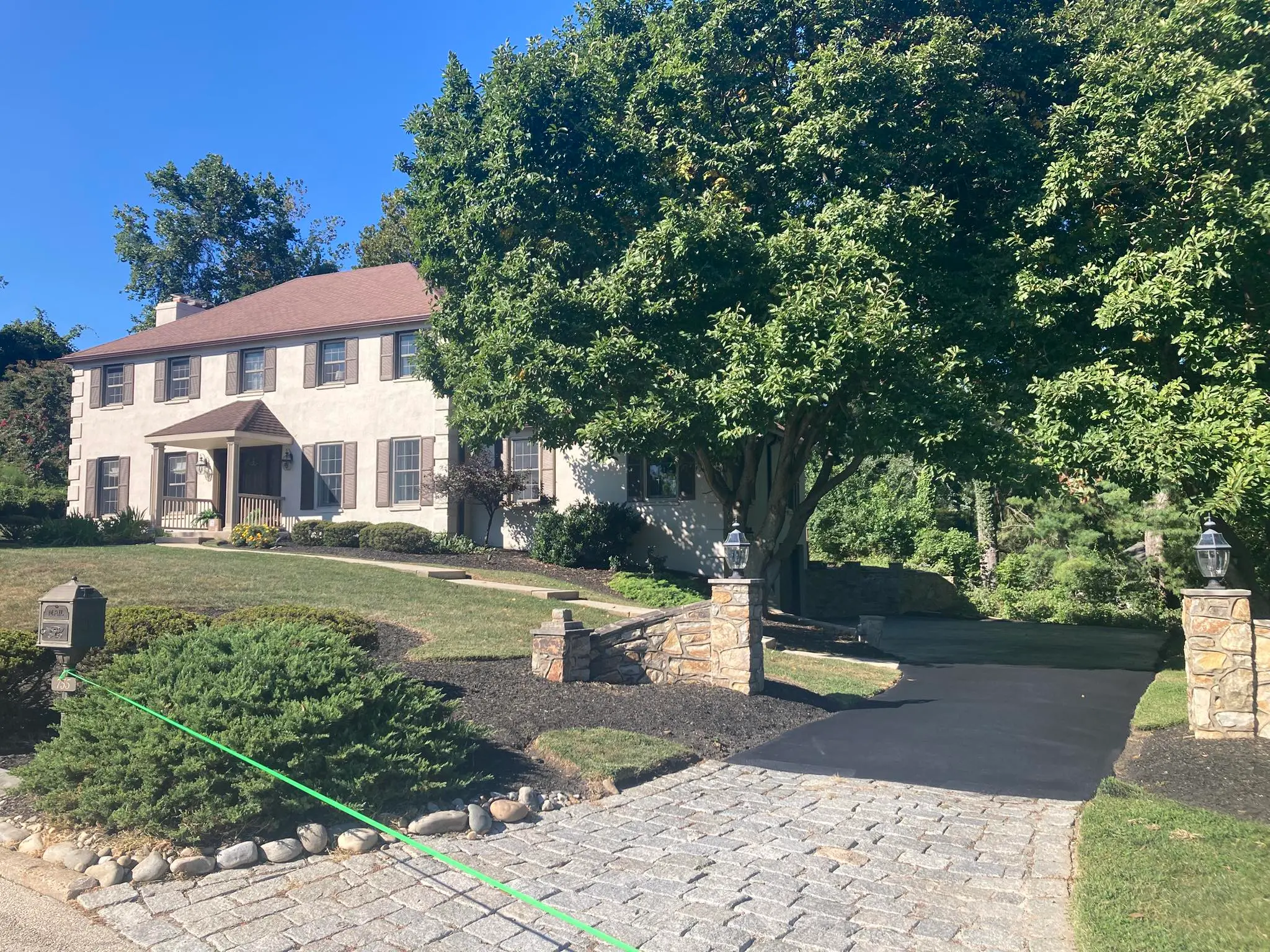 A stucco colonial with a sealcoated asphalt driveway meeting a cobblestone apron at a clean, straight line.